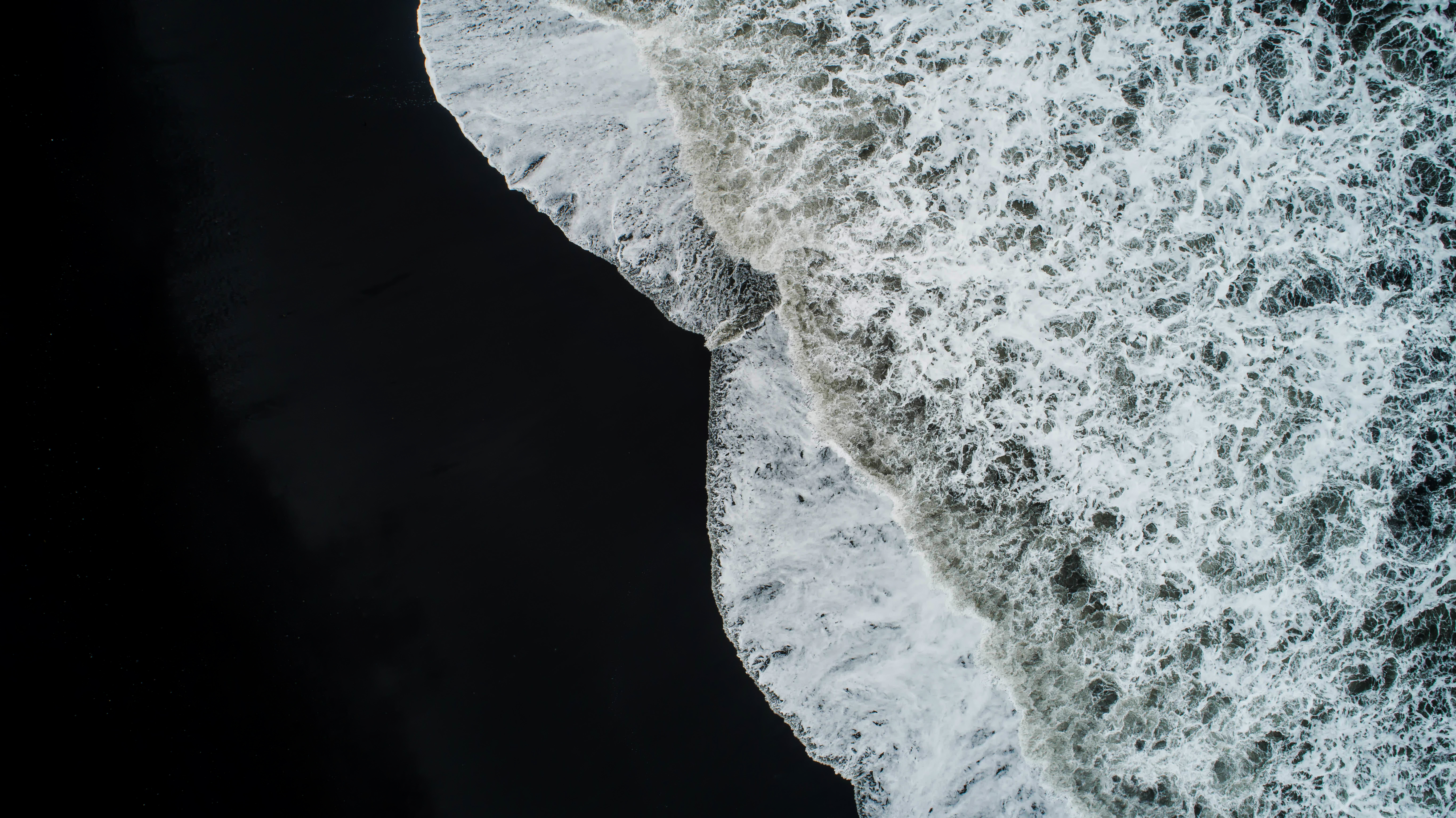 Ein schwarzer Strand mit weißem Wellenschlag